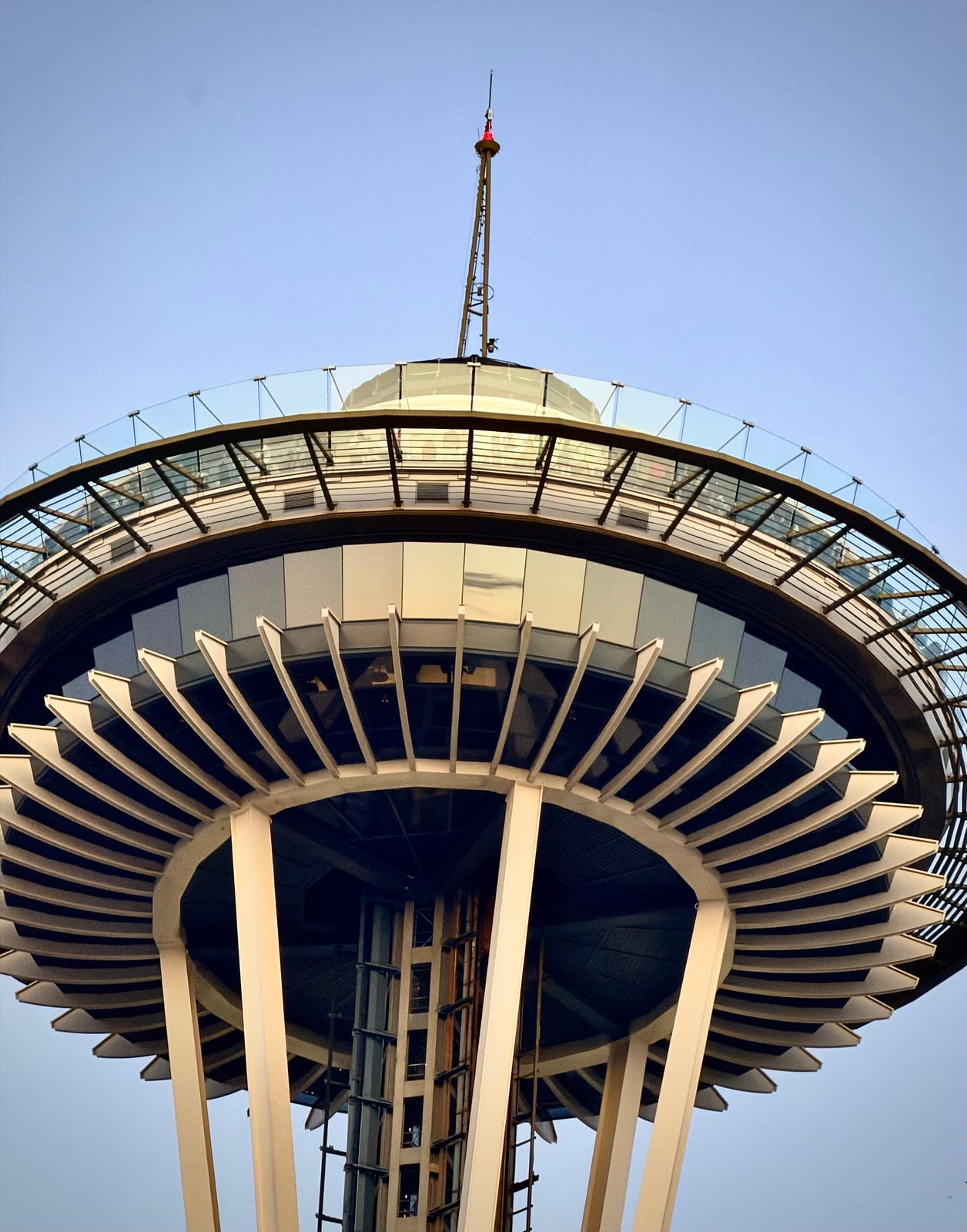 Looking up at the Space Needle's circular observation deck and spire against a pale blue sky