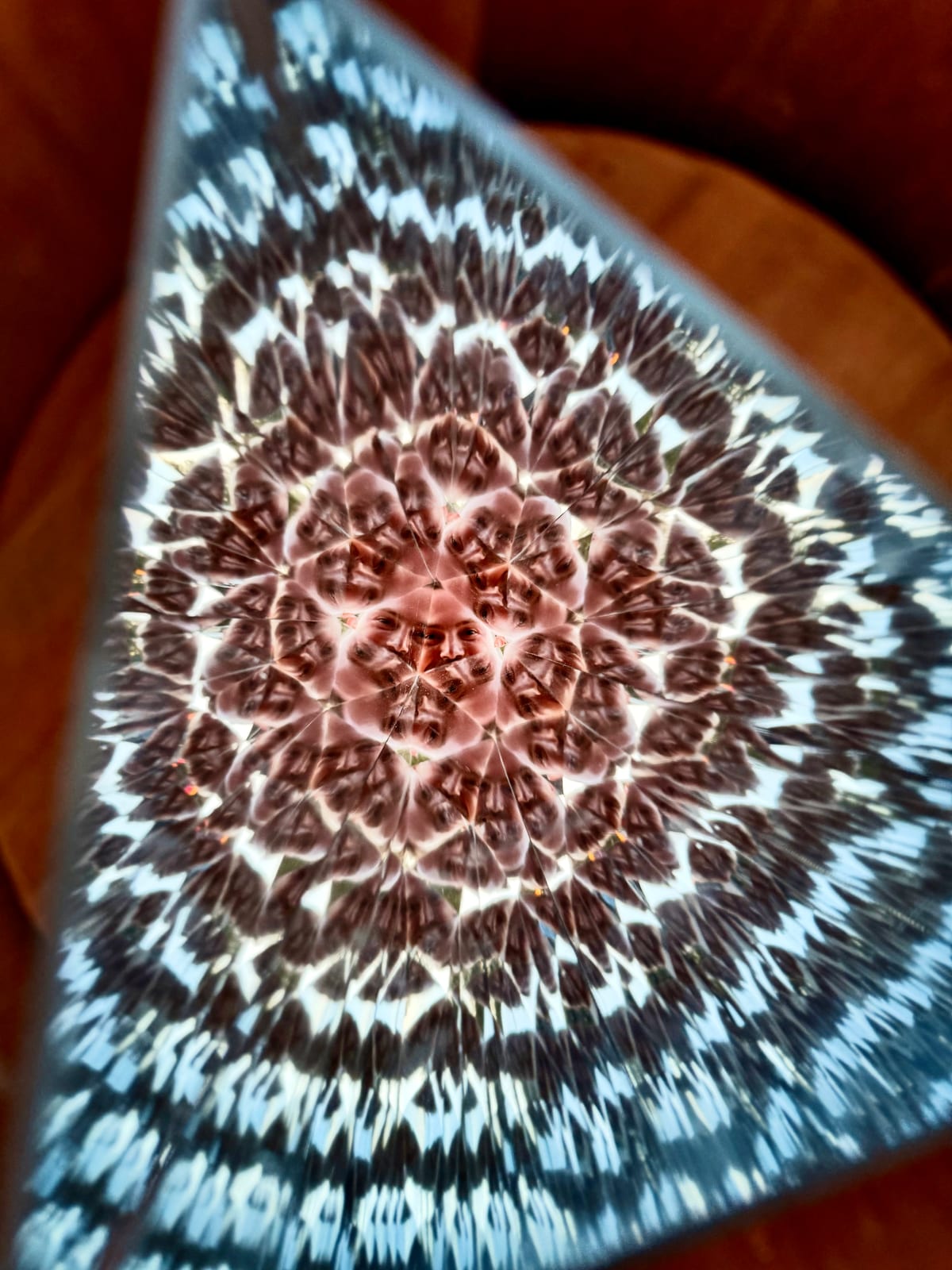 A face repeated in a kaleidoscopic pattern of reflections inside a triangular mirrored opening
